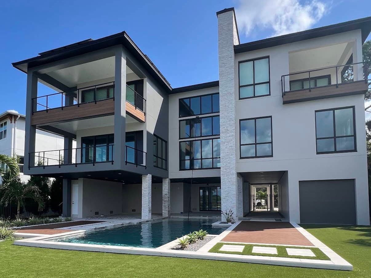 A modern three-story home with walls of glass above a pool, a water-fed pole at the windows