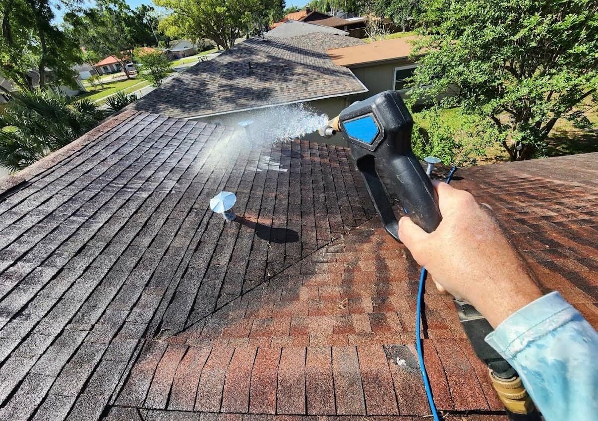 A shingle roof being soft washed with a low-pressure sprayer