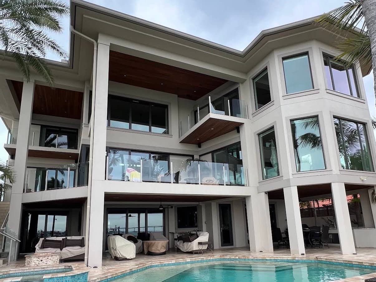 A three-story waterfront home with walls of glass above a pool deck